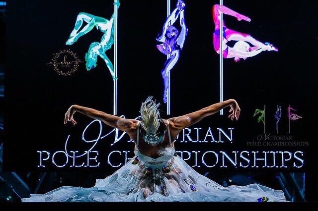 woman on stage in bird costume with feathers performing pole dancing routine at Victorian Pole Championships