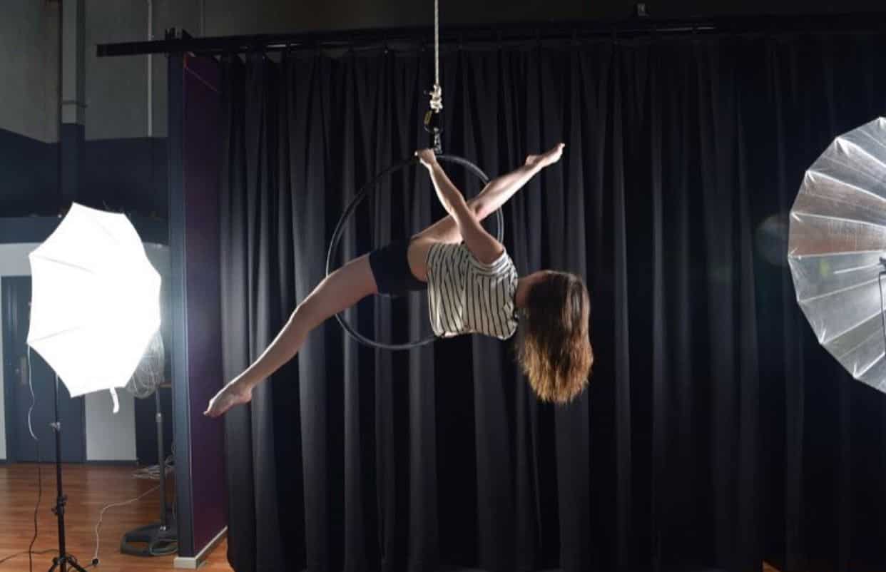 woman training aerial hoop for photoshoot under big lights doing split, aerial silks, aerial silk classes, aerial classes