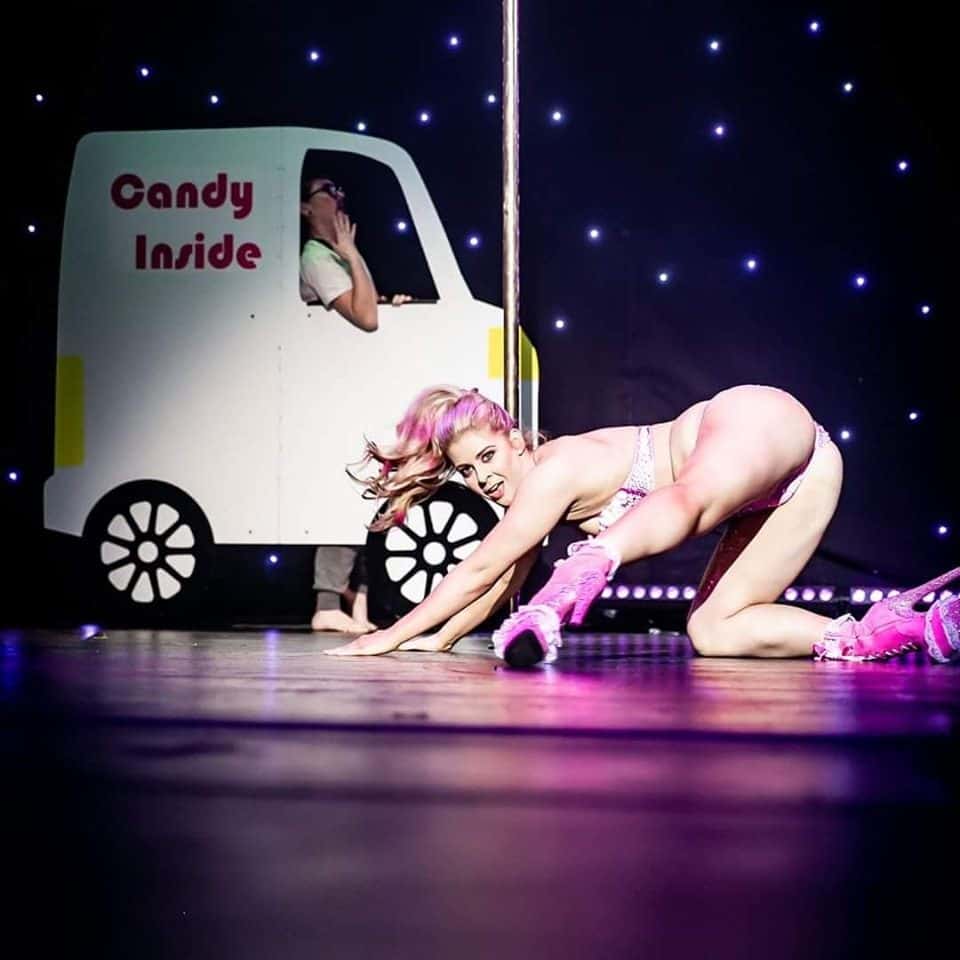 woman on stage performing wearing pink heels and outfit in front of pole, pole fitness, pole dancing