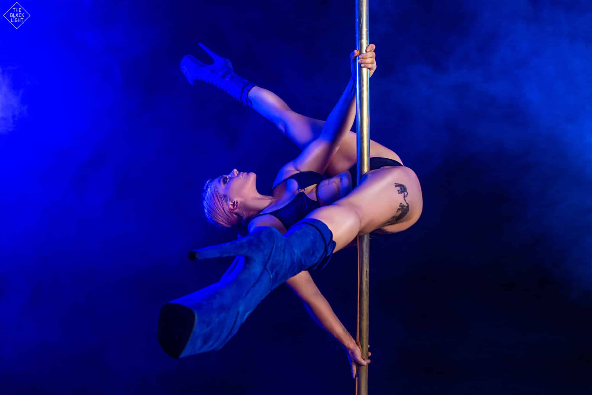 woman on pole in split trick wearing heels under blue lights for photoshoot