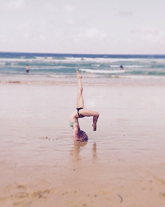 woman oj beach doing yoga headstand pose for photo