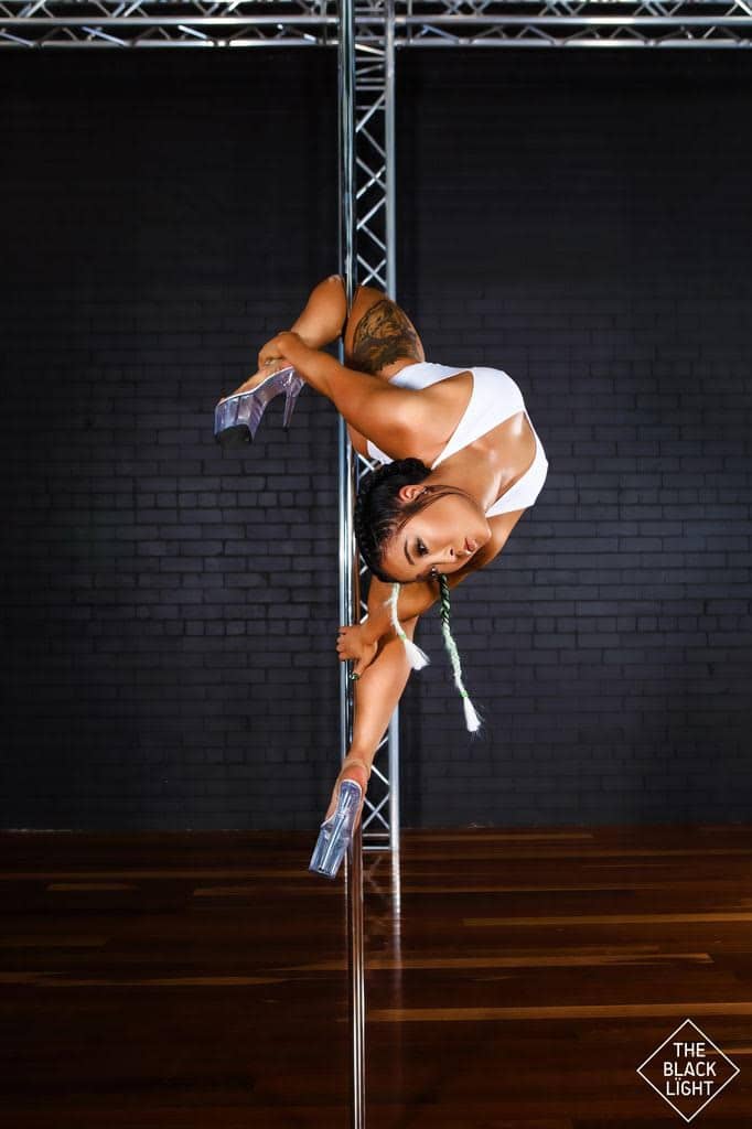 Woman on pole doing twisty trick bendy back in eight inch heels. pole fitness, pole dancing