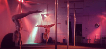 video image of woman training dynamics on pole at studio under pink lights
