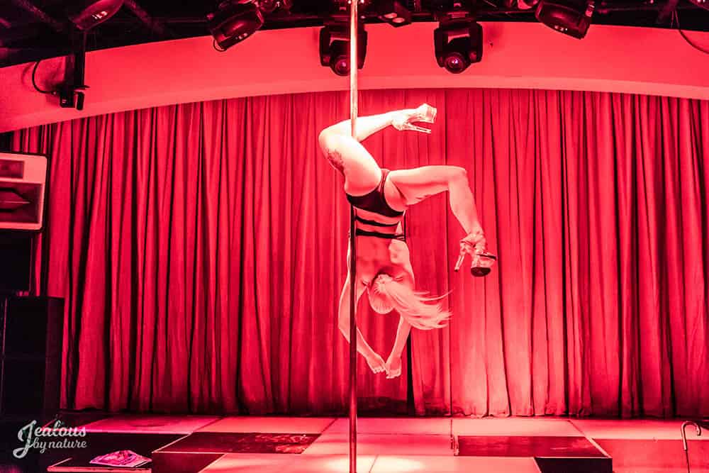Woman performing in pole competition red colour lights upside down trick, pole fitness, pole dancing